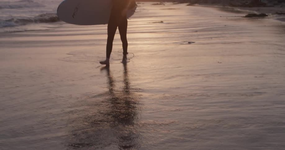 A man walks across the shallow water holding a surfboard