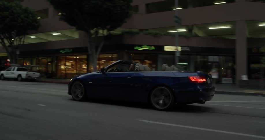 A blue convertible driving down a road in a city