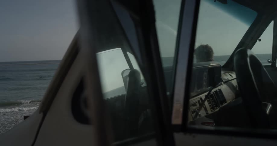 A man with a surfboard walks past a car