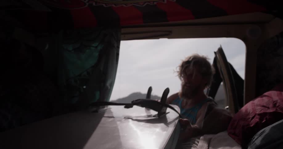 A man opens the car door and takes out his surfing gear