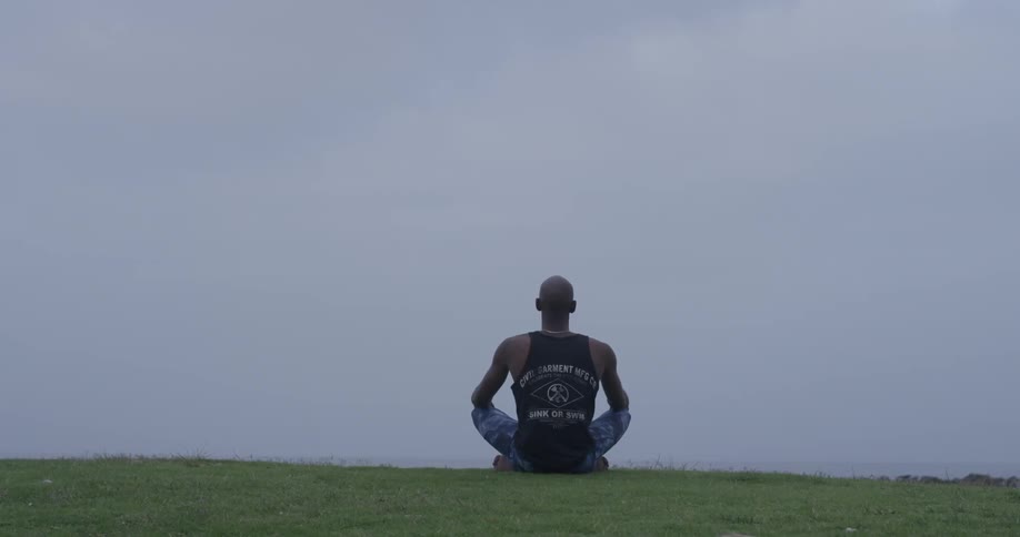 A man sitting cross legged facing the cloudy sky