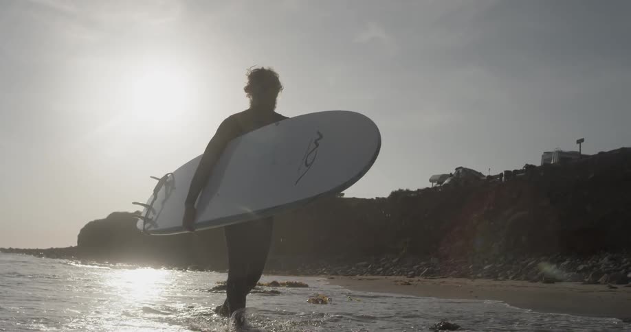A man holding a surfboard walking through waves crashing onto the beach