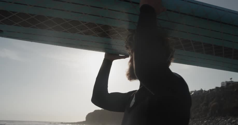 Man walking into the ocean with a surfboard on his head
