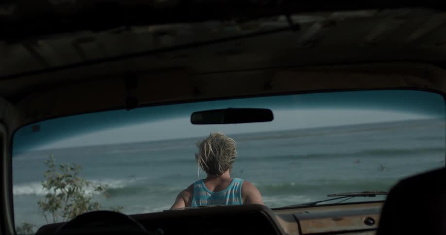 A man standing in front of a car at the ocean