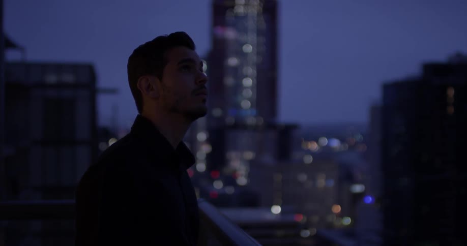 A man standing on a balcony looking at a city at night