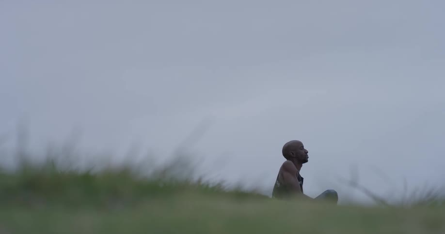 A man walks outside in the grass and sits down