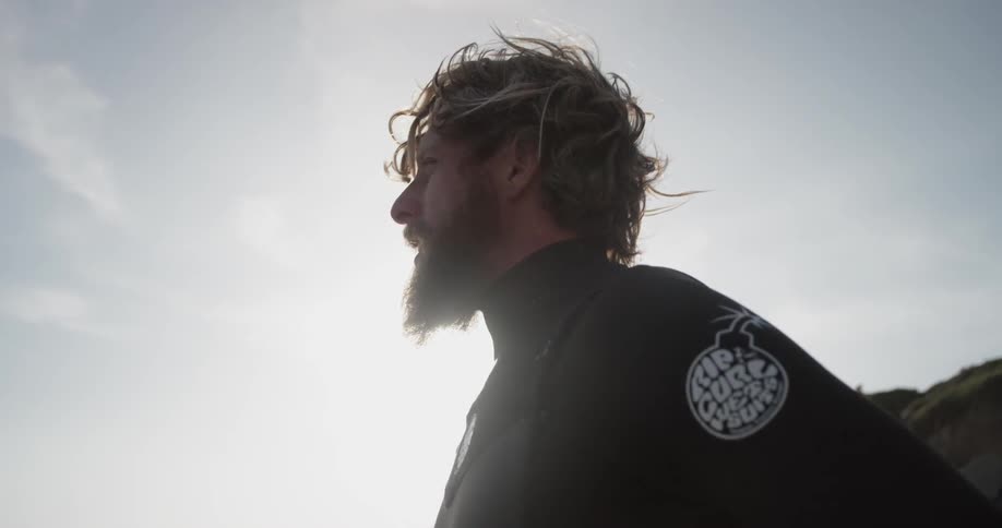 The top half of a man wearing a wet suit and looking out at the ocean