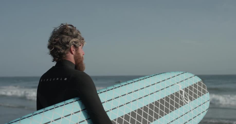 A man holding a surfboard looks out to the water