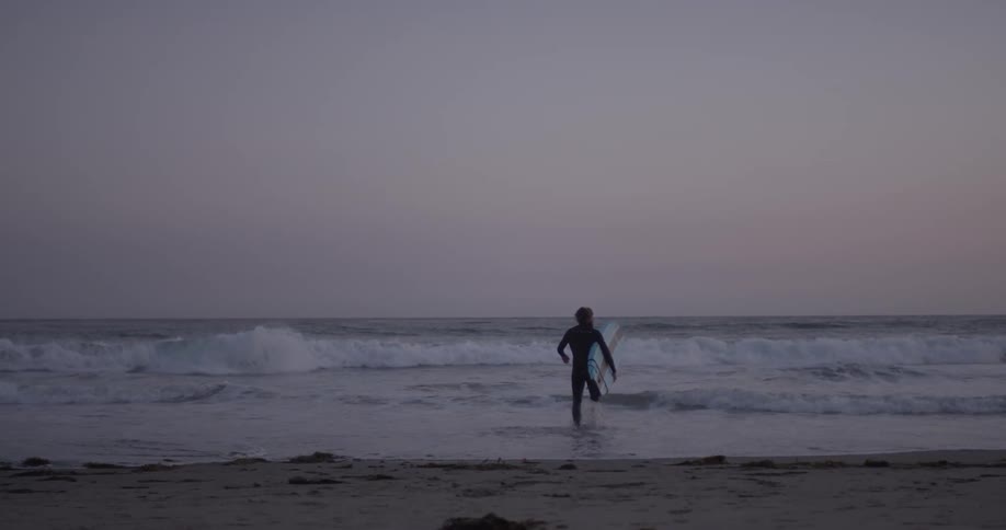 A surfer carries his surfboard into the water