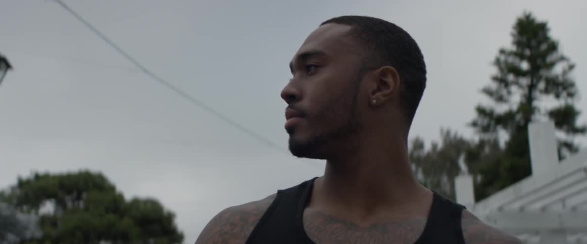 Man looks into the camera while standing outdoors on a cloudy day