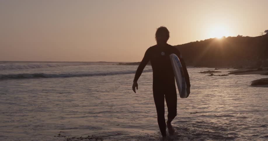 A man wearing a wetsuit and carrying a surfboard at night