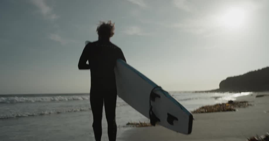 A man picking up a surfboard and walking toward the sea