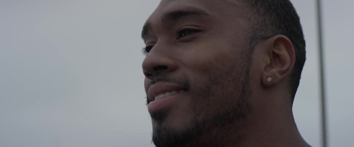 Man leans against a fence and smiles on a cloudy day
