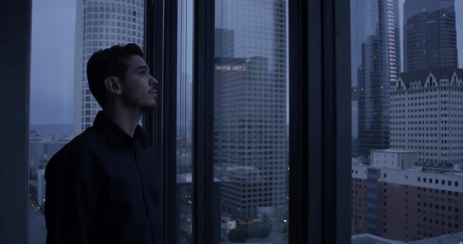Man looks pensively out of window from tall building
