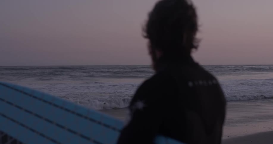 A man wearing a wetsuit holding a surfboard at sunset