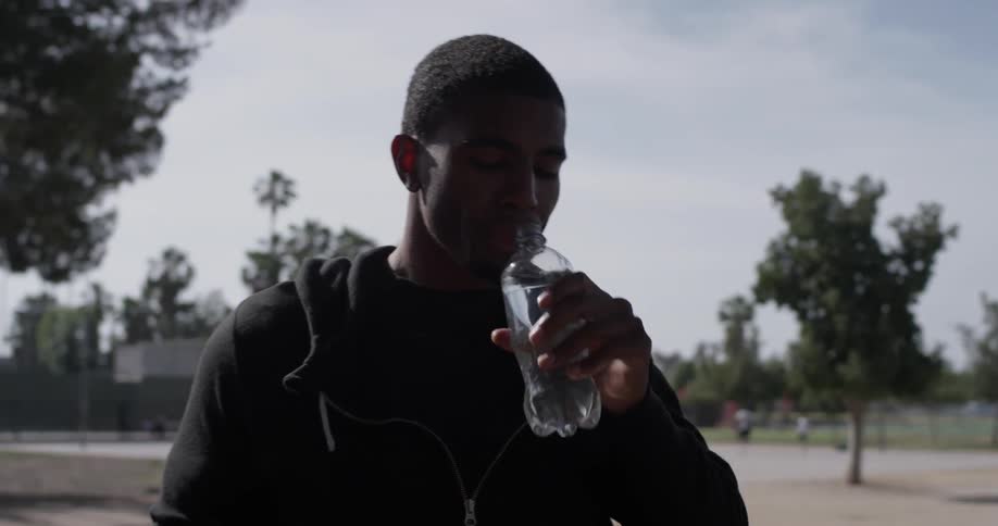 A man walking down a sidewalk taking a sip of water from a bottle