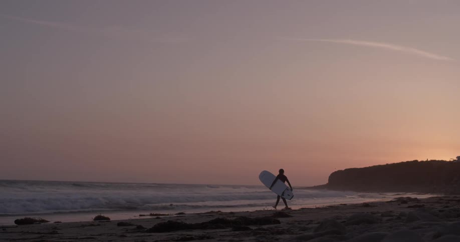 A man carrying a surfboard towards the sea at sunset