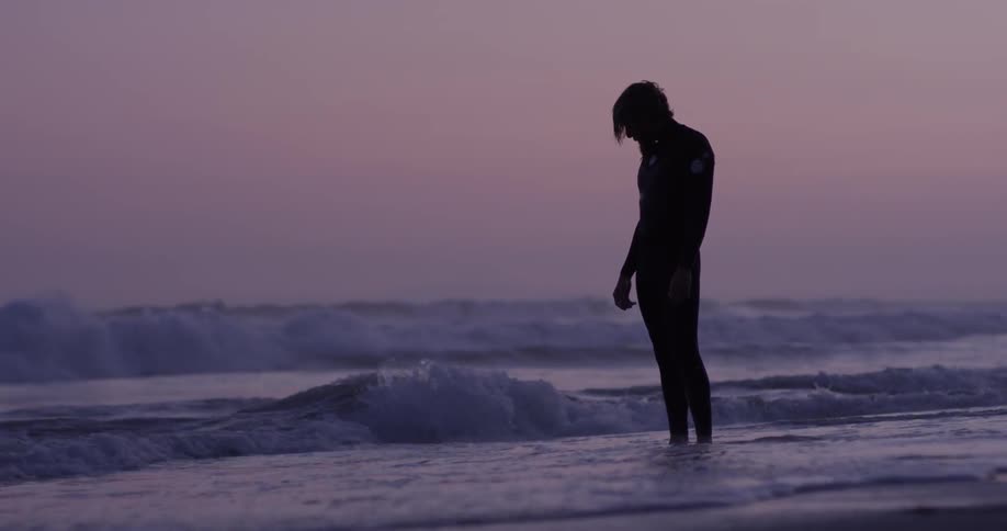 A man standing on the edge of the water with waves crashing at his feet