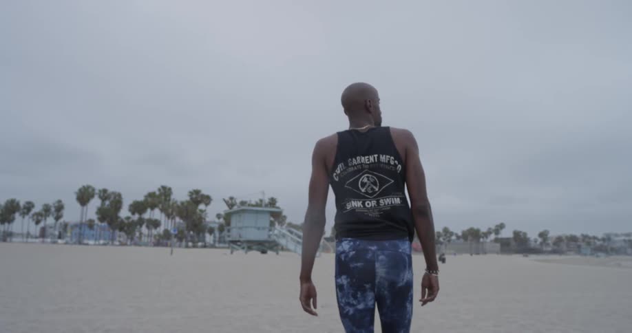 A man in leggings and a tank top walks on the beach