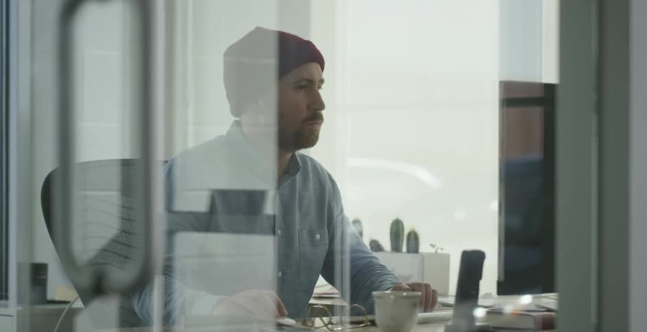 A man works at a computer in a glass walled office