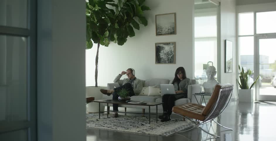 A man and a woman sitting on a couch each working on laptops