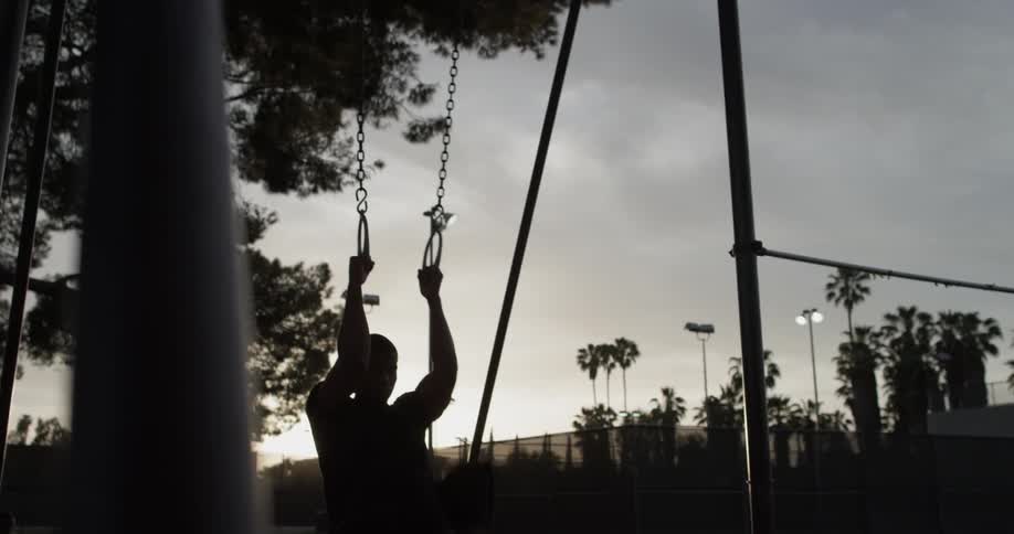A man swinging his legs while holding gymnast rings