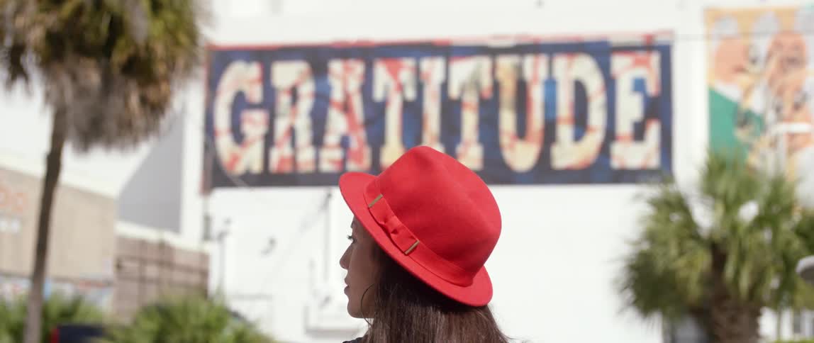 A young woman, who is wearing a red hat, looks off to her side before turning to face forward