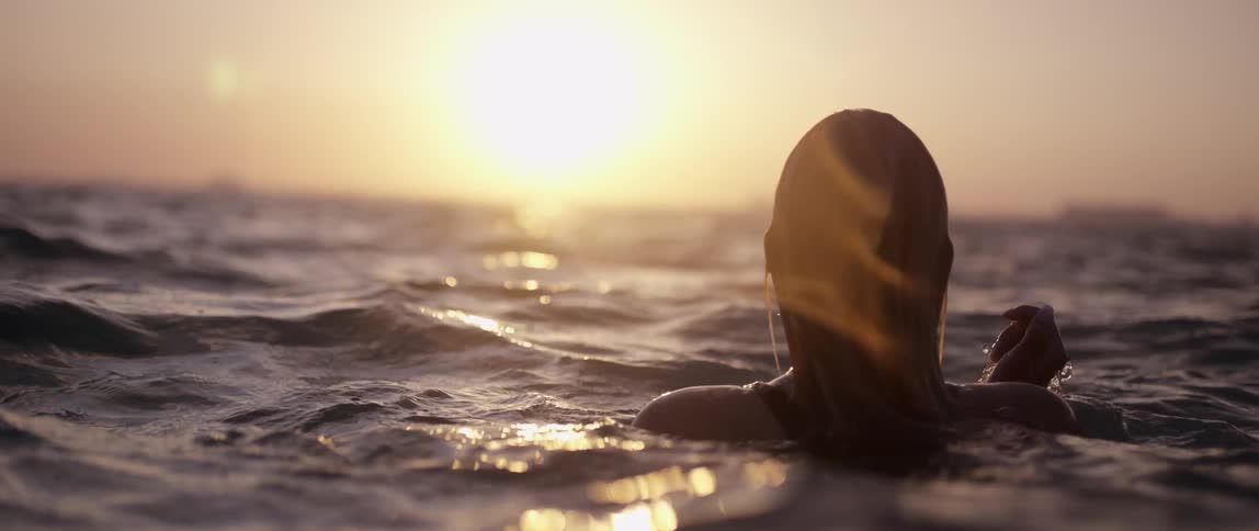 A woman emerges from gently rolling ocean waves at sunset