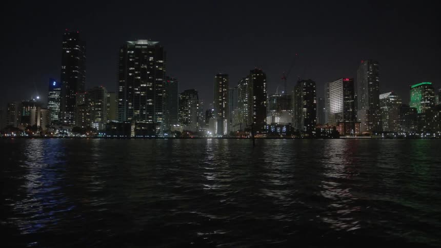 A body of water in front of skyscrapers at night