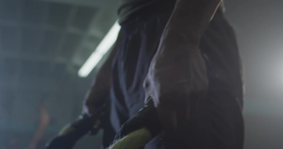 A muscular man bends over and picks up two ropes with one in each hand