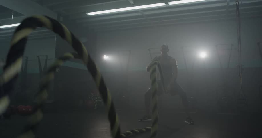 A man is shaking large ropes against the floor