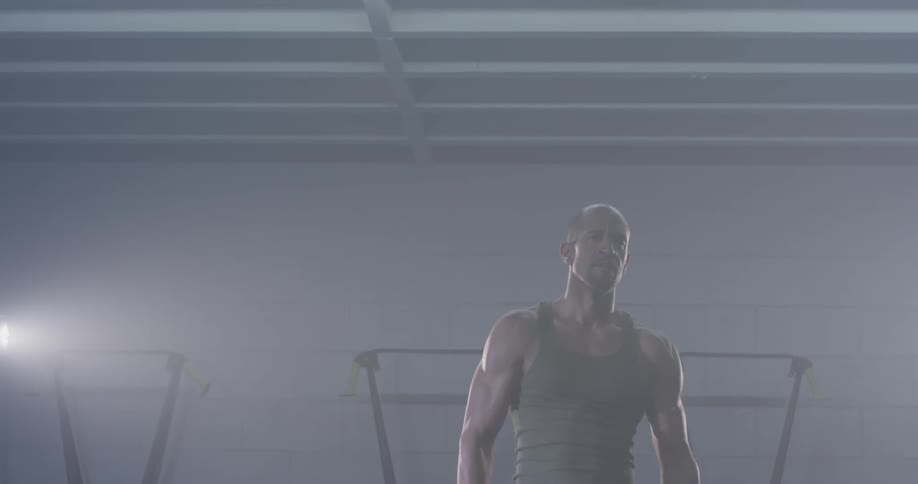 Man in a tank top stands in a dimly lit gym and walks away