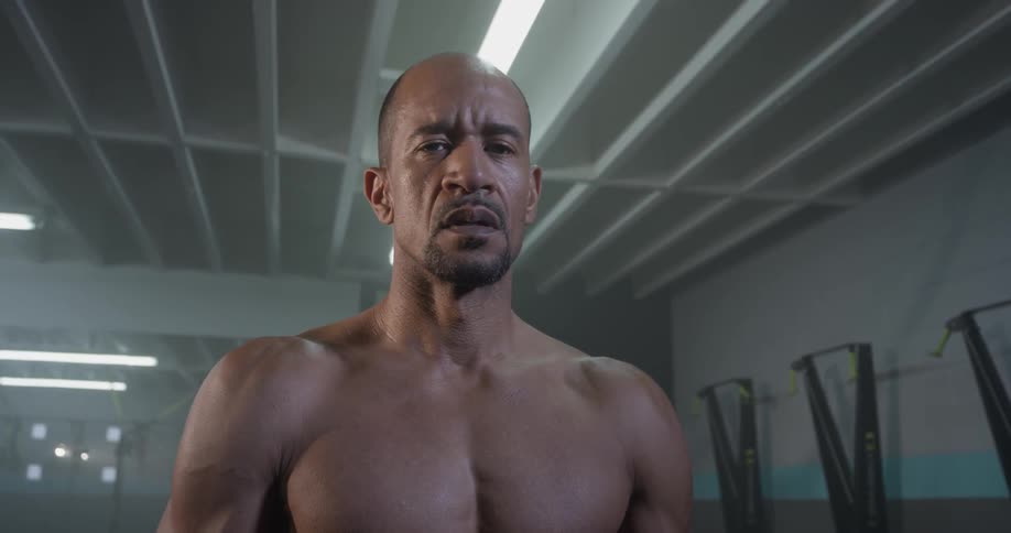 Shirtless man breathes heavy and stares straight ahead in a gym