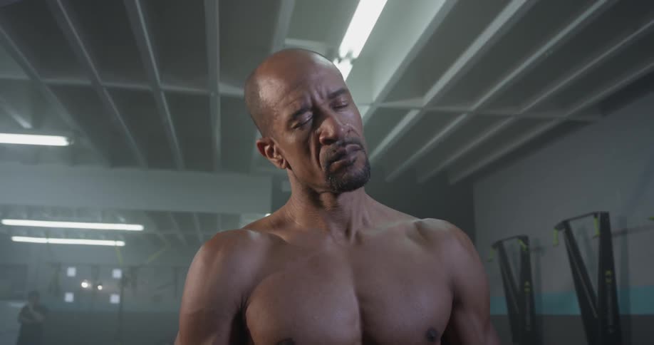 Shirtless man stretches in gym