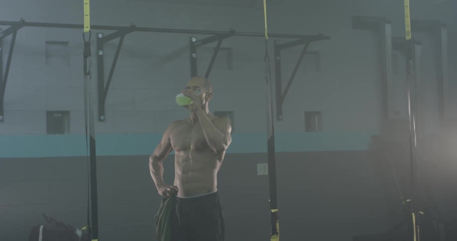 A muscular man takes a drink then closes the container