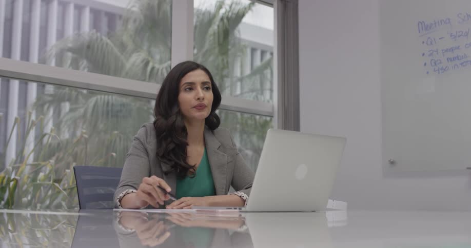 A woman is writing on a piece of paper by a laptop