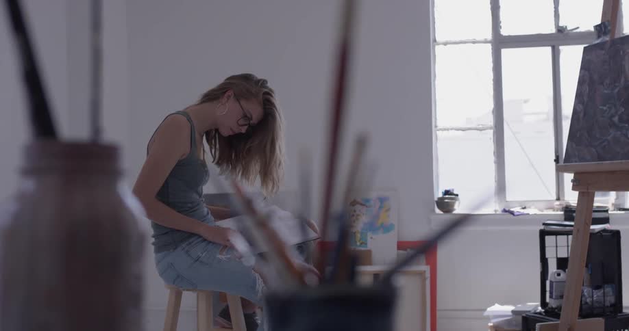 Woman draws in background of cup with paintbrushes in it