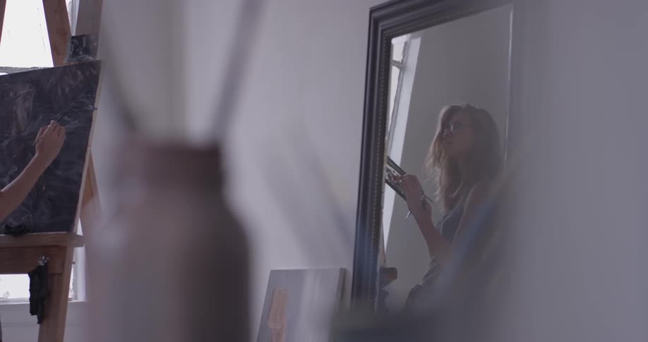 A woman is seen painting in the reflection of the mirror