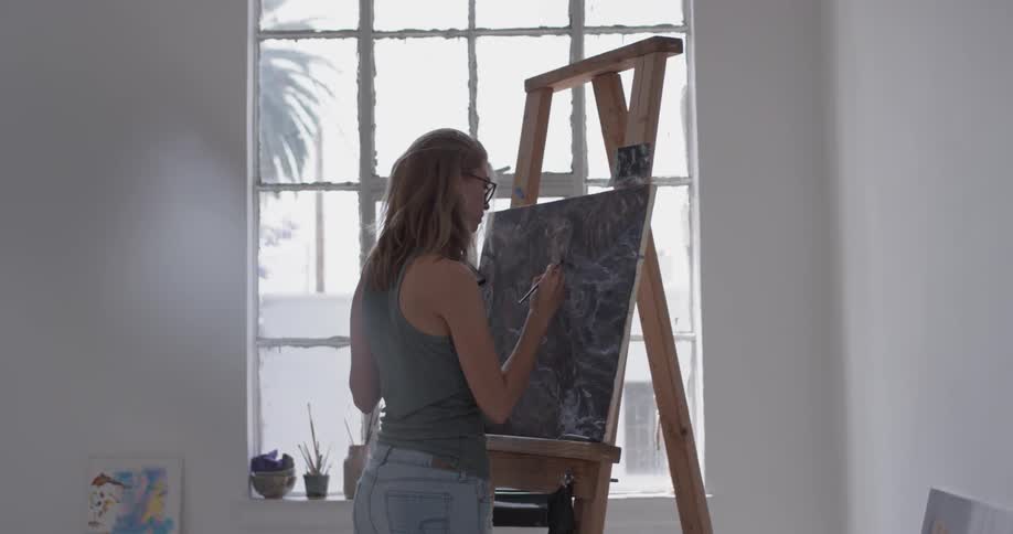 Woman paints on a canvas next to a window