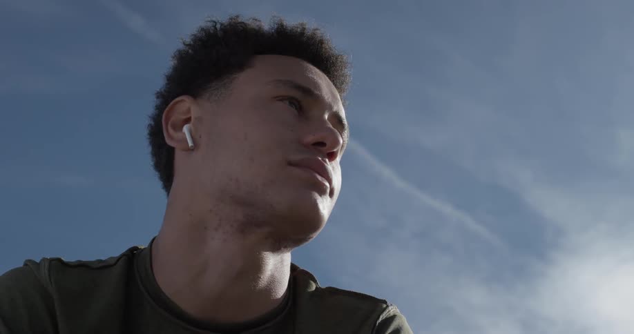 A man is wearing earbuds as we see the blue skies with contrails and clouds on a blue sky sunny day