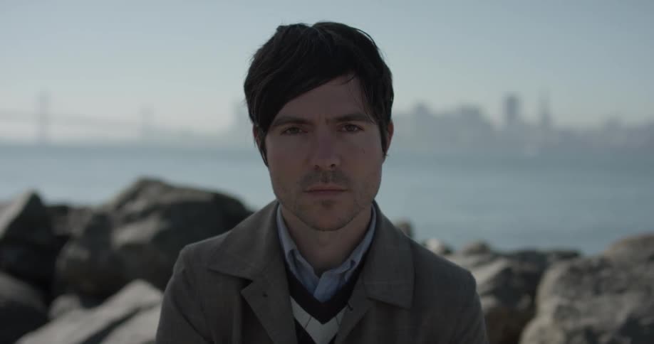 Man sits near rocks and stares ahead at camera