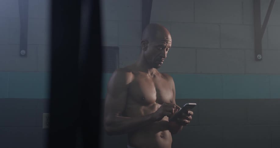 A shirtless man look at his cell phone