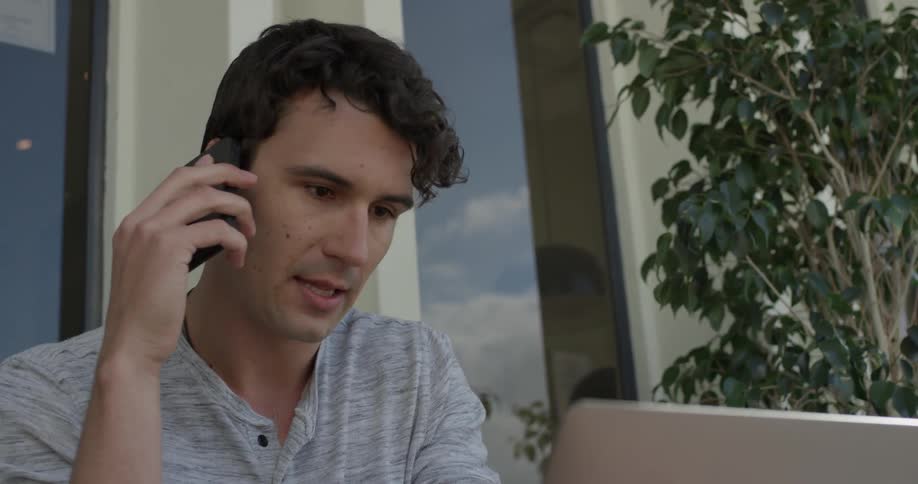 Man talks on a phone looking at his laptop