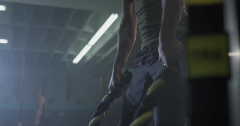 A man bends down to pick up large ropes and starts to shake them