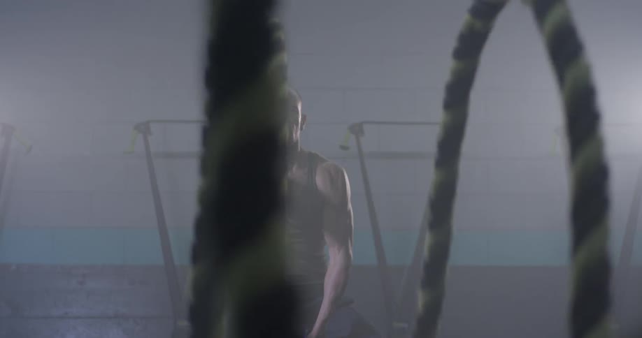 A man swinging ropes in a gym