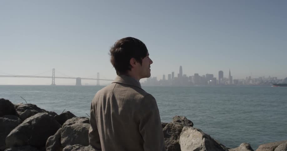 Man standing at the shore looking at a city in the distance