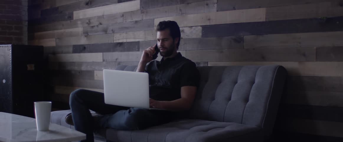 A man is talking on the phone while looking at a laptop