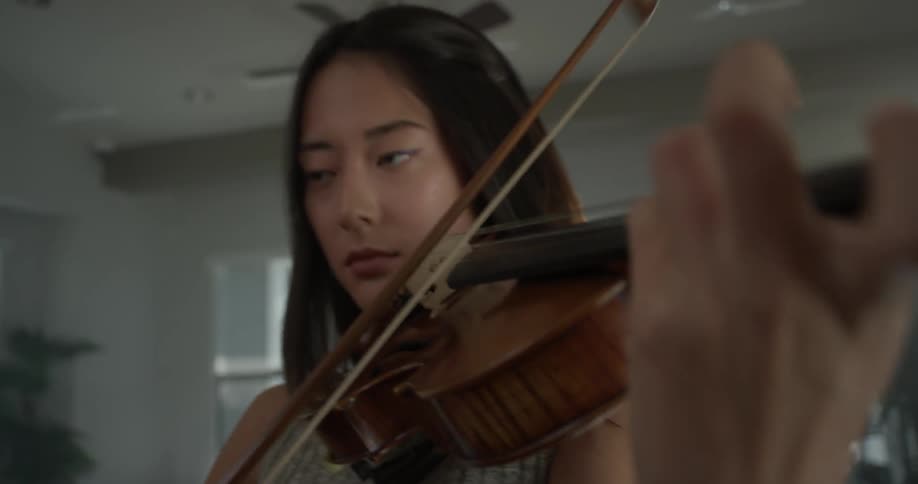 A woman stares off to the distance while playing the violin