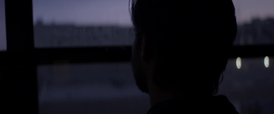 Man in dark room looks out of window at dark city