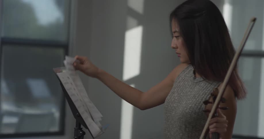 A woman carrying a violin and setting up sheet music on a music stand